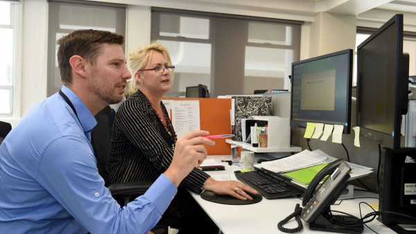 A man and a woman at a desk talking and working together at a computer