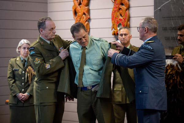 Willi Apiata getting a warrant officer jacket placed on him by two men in miltary uniforms